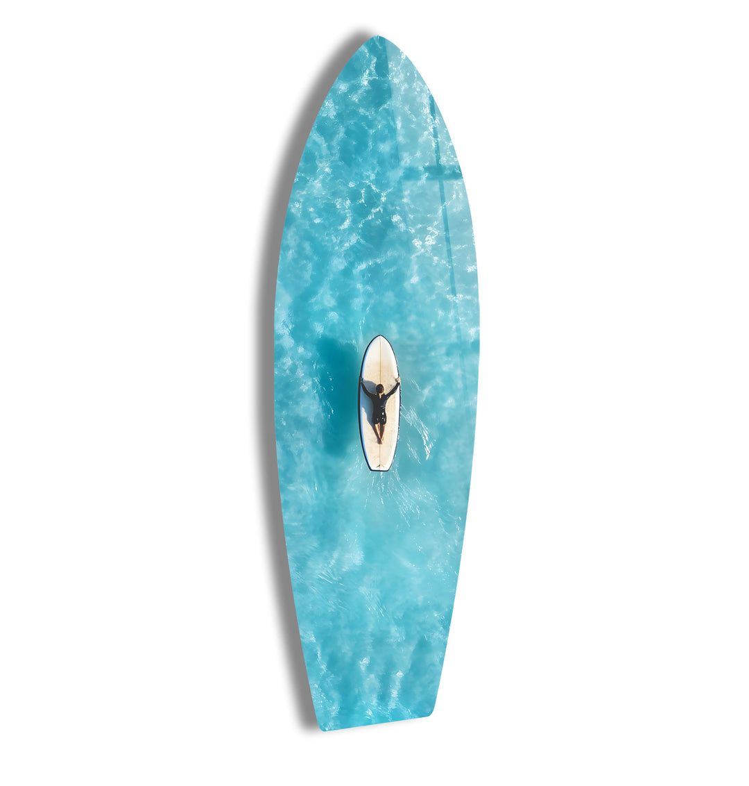 Aerial view of a surfer gliding through clear turquoise waters, captured on stunning glass wall art.
